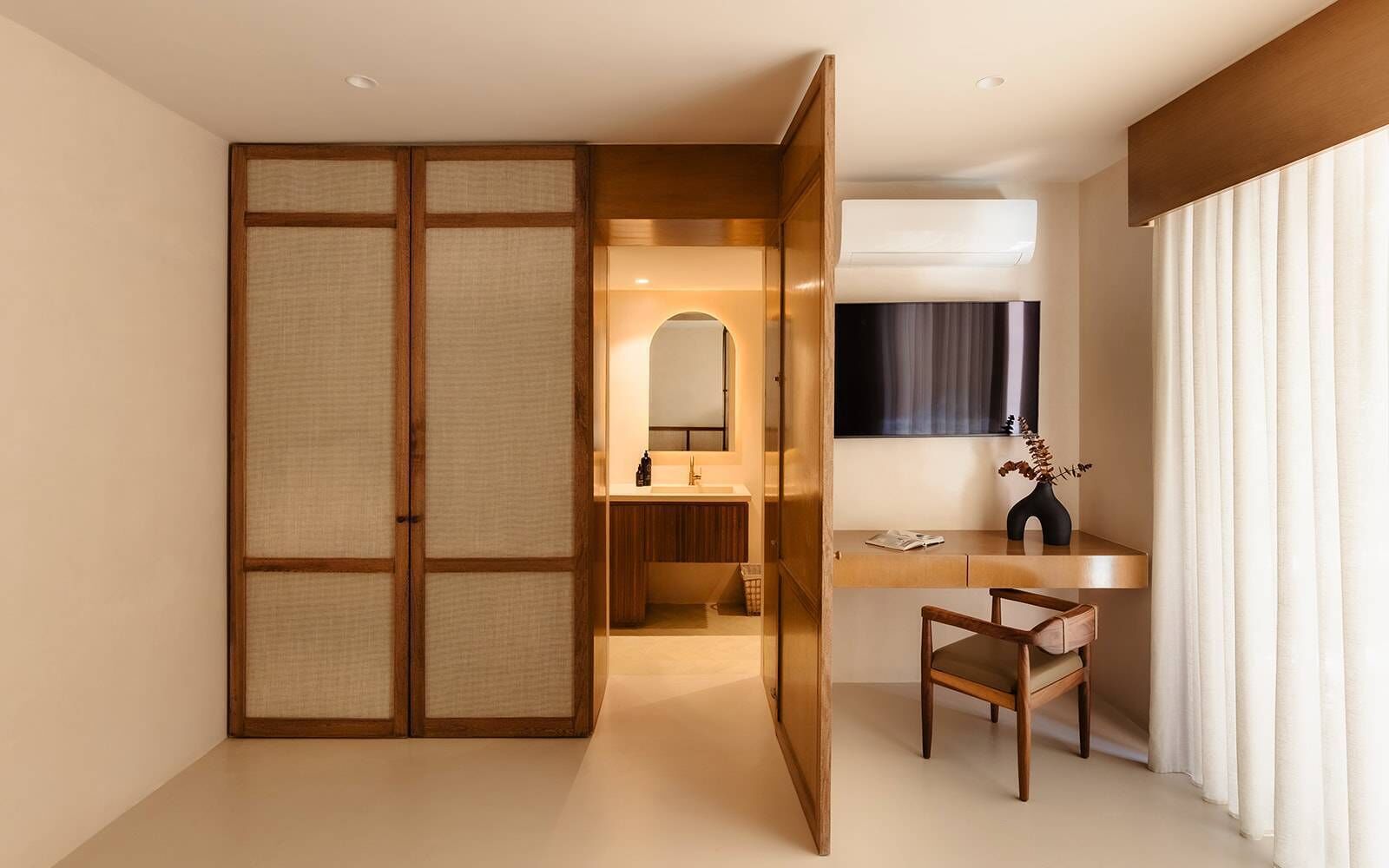 A hotel room with a sliding shoji screen door, a desk with a chair, a mirror, and an air conditioning unit.