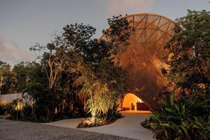 A structure with a lattice design, surrounded by dense foliage and a paved pathway leading to it. - Aflora Moon 3 bd First FloorBeach Club + Breakfast (Tulum)