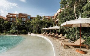 Ein Poolbereich mit Liegestühlen und Sonnenschirmen, umgeben von Grünflächen und Hotelgebäuden.