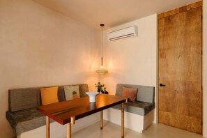 Ein Zimmer mit einem Holztisch, einer Couch mit Kissen, einer Pendelleuchte und einer Holztür.