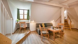 En rummelig opholdsstue med trægulv, sofa, spisebord med stole og en trappe til et højere niveau.