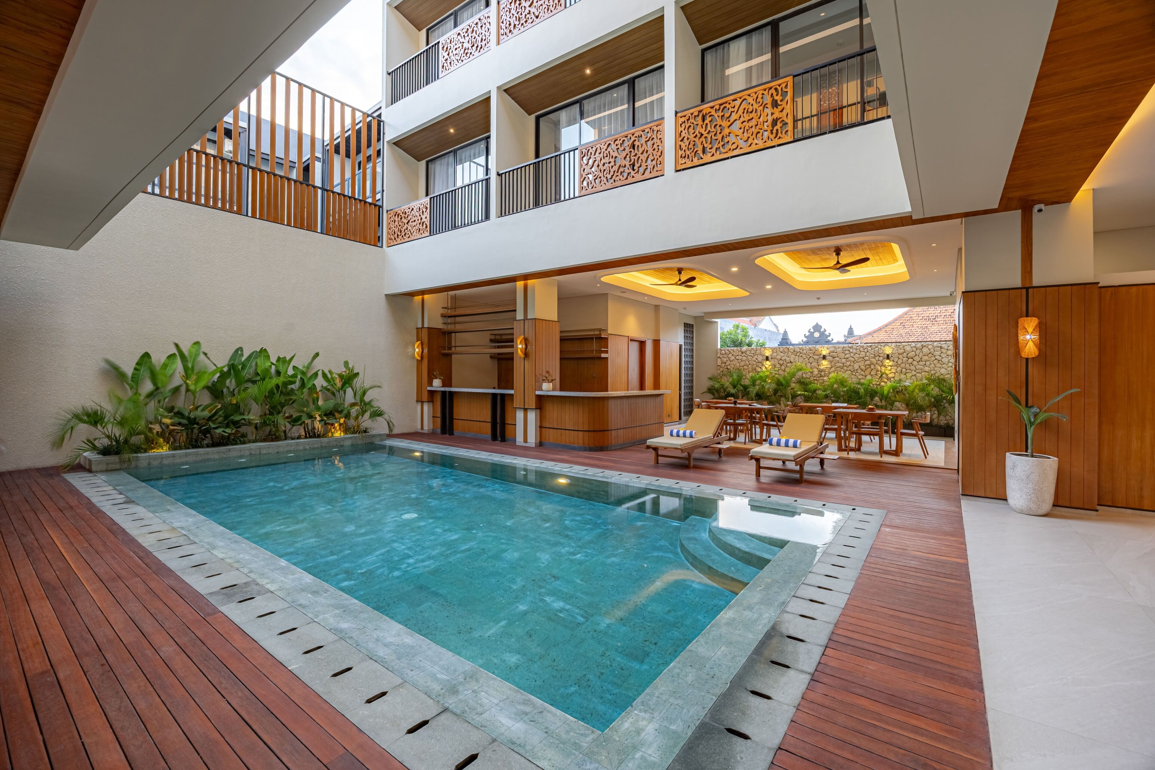 Ein moderner Innenpoolbereich mit Holzterrasse, Liegestühlen und Blick auf die umliegende Architektur.