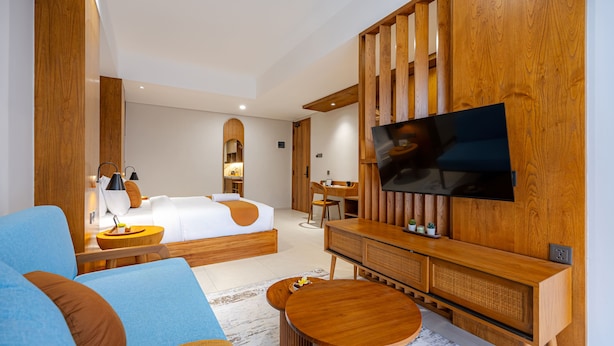Une chambre d’hôtel moderne dotée d’un grand lit, d’un téléviseur fixé à un mur en bois, d’un coin salon avec un canapé et une table basse, ainsi que d’un bureau avec une chaise.