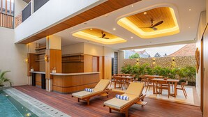 Un espace piscine extérieur moderne, doté de chaises longues en bois et d’un bar.