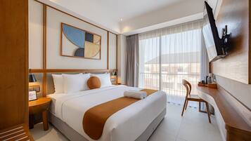 Habitación de hotel con una cama grande, un escritorio, una silla, un televisor y una ventana con cortinas.