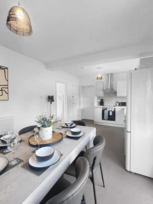 A modern kitchen with white cabinetry, a dining area with a wooden table set for four, and a hanging pendant light.