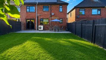 A two-story brick house with a well-maintained lawn, a patio with outdoor furniture, and a black fence surrounding the property.