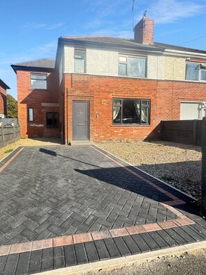 A two-story brick house with a paved driveway and a small garden area.