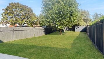 Een achtertuin met gras, een boom en een houten omheining.