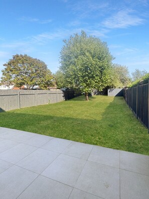 A backyard with a lawn, a tree, and a wooden fence.