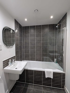 A modern bathroom with a freestanding bathtub, a wall-mounted sink, and a mirror. - Liverpool City View 1-Bed Apartment (Liverpool)