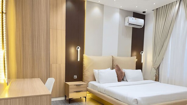 Ett modernt hotellrum med en säng, sängbord, ett skrivbord och en luftkonditioneringsanläggning.