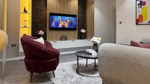 Ett modernt vardagsrum med en platt-TV som är monterad på en väggpanel i trä, en röd fåtölj, ett runt soffbord med böcker och en vas med blommor.