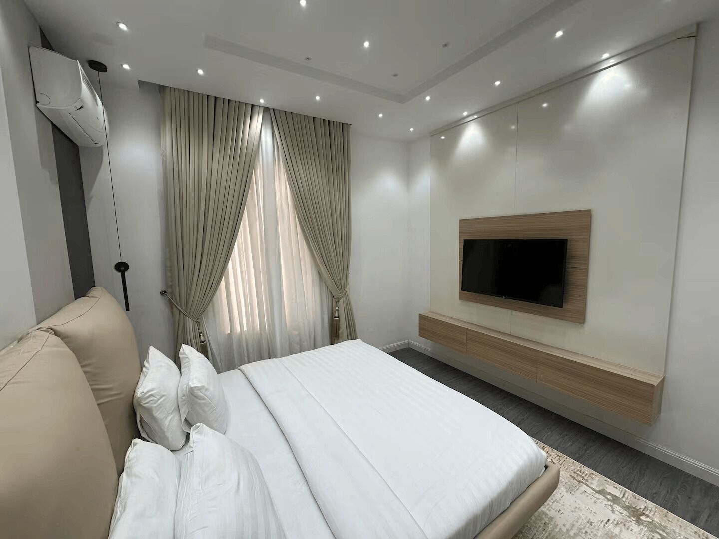 A modern bedroom with a bed, a TV mounted on the wall, and a large window with curtains.