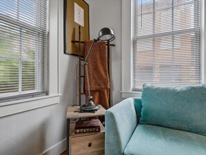 Une pièce avec une fenêtre, un bureau avec une lampe, un canapé et une étagère fixée au mur.