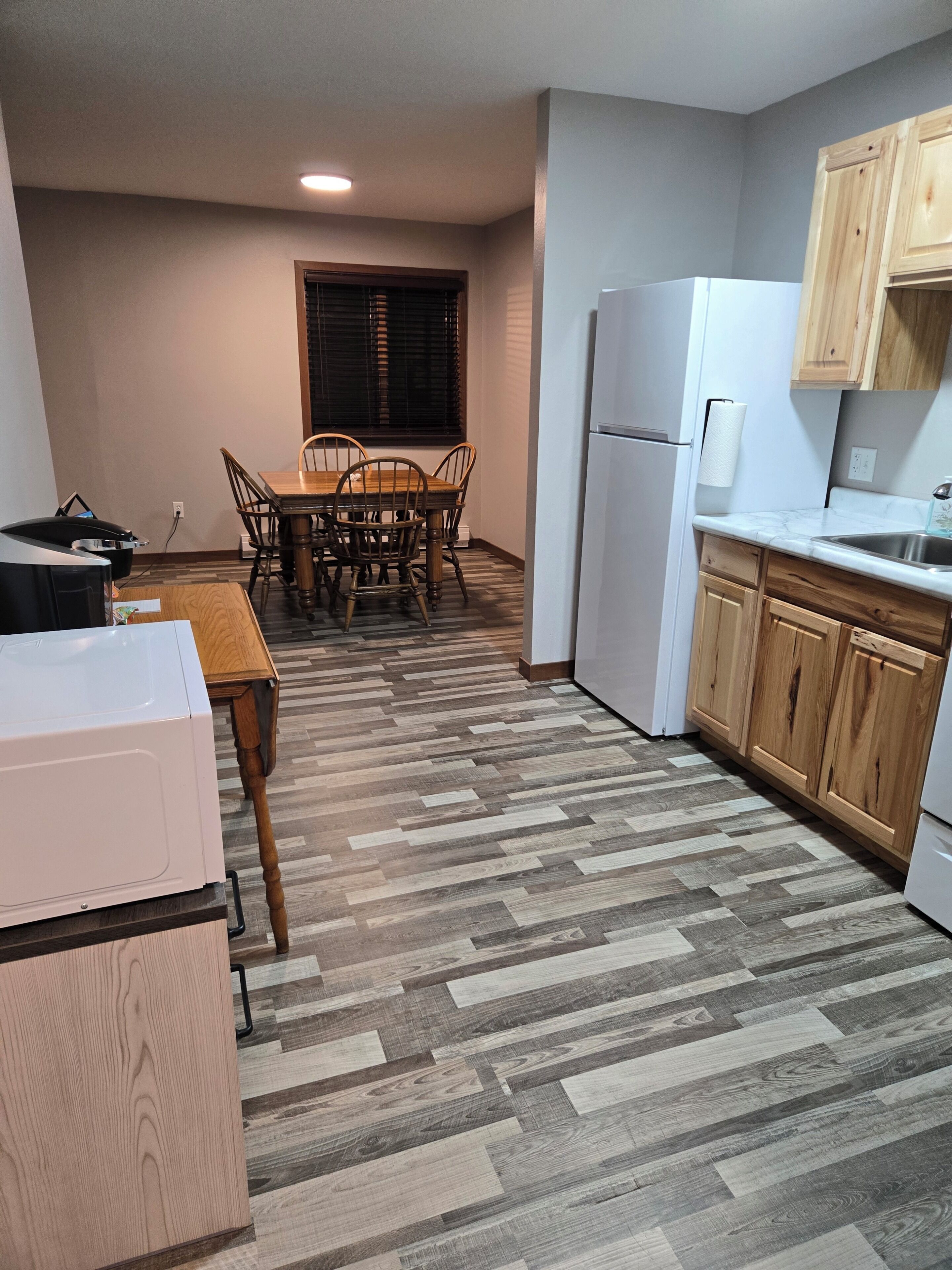 A compact kitchen with a dining table, wooden chairs, a refrigerator, and wooden cabinets.