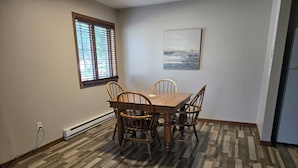 Un comedor con una mesa y sillas de madera, una ventana con persianas y un cuadro en la pared.