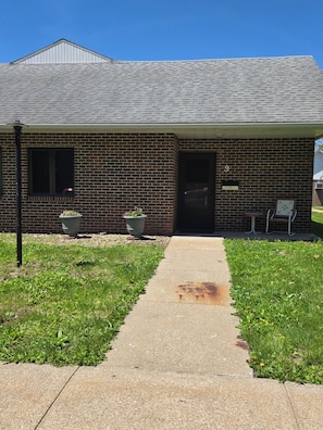 A single-story brick building with a covered porch, a visible number '9' on the door, and a concrete pathway leading to the entrance.