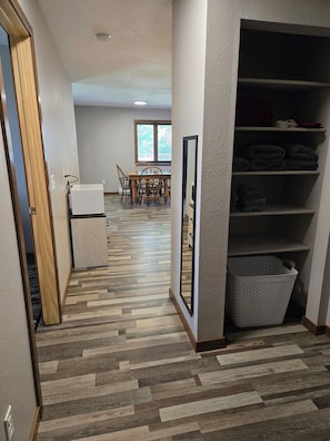 A hallway with a wooden floor, a dining area with a table and chairs, and a storage unit with shelves and a basket.