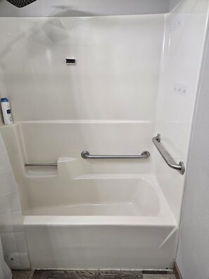 A white bathtub with a grab bar, a handheld showerhead, and a bottle of shampoo.