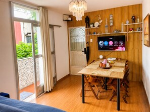 A room with a wooden dining table, chairs, a TV mounted on the wall, and a window with curtains. - Rio Complete Beach, Samba & Carnival 1 (Rio de Janeiro)