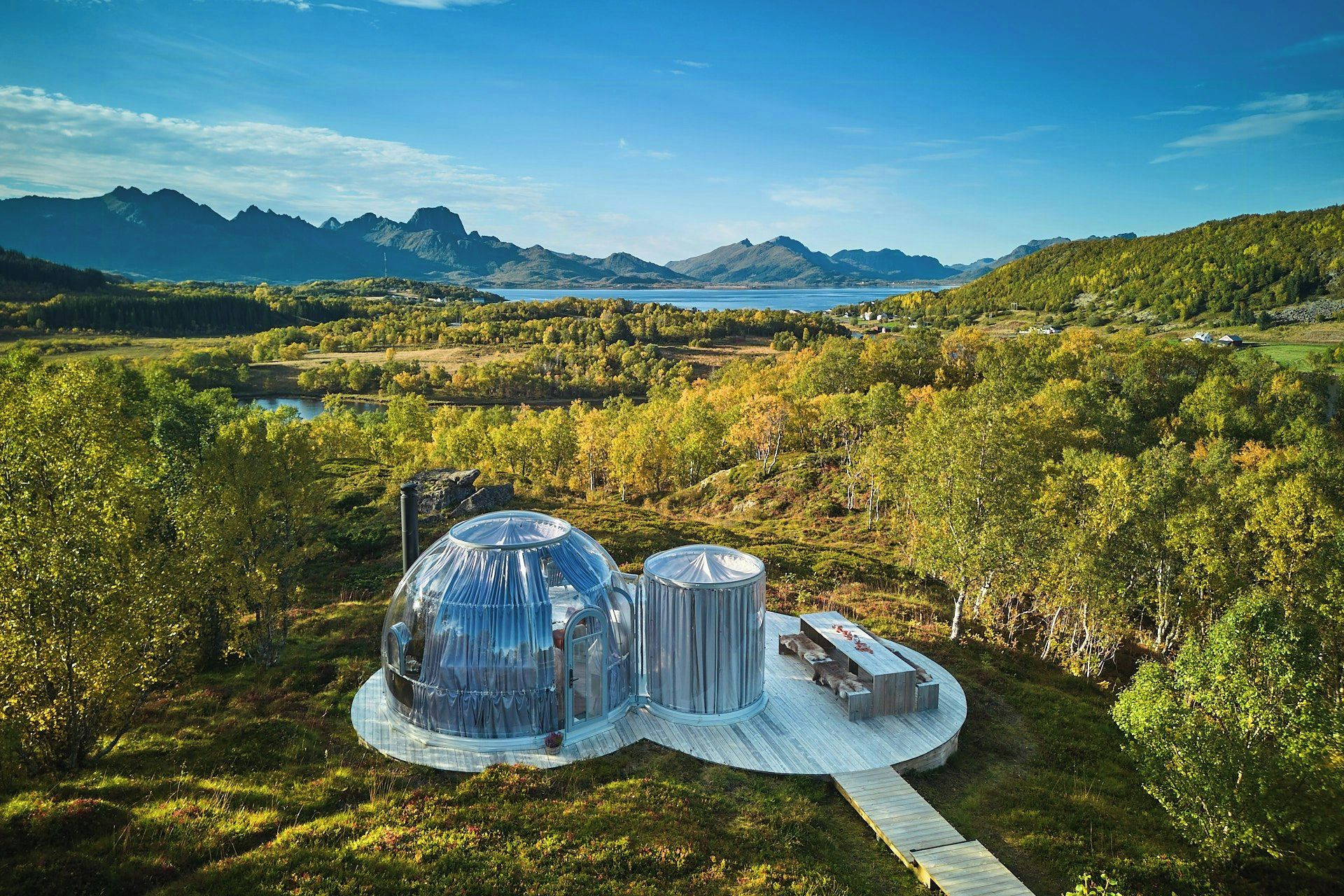 Una cabana isolada amb una estructura de cúpula transparent, envoltada per un bosc i muntanyes.