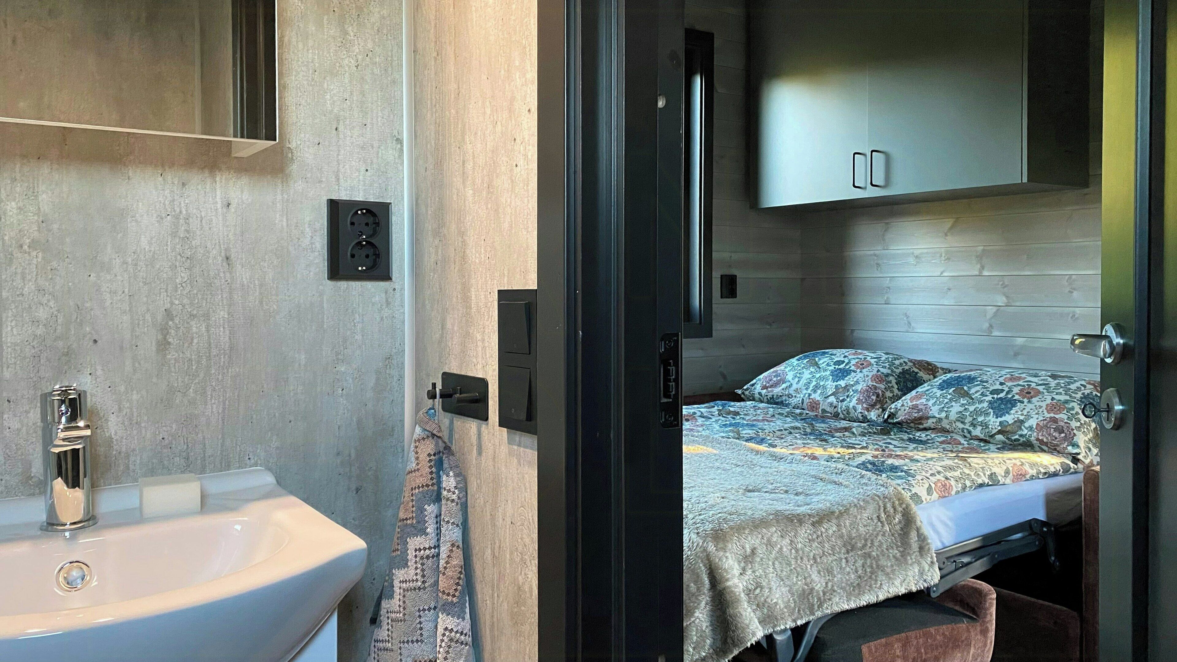 Habitación funcional con cama, armario empotrado, lavamanos y una toalla colgada en la pared.