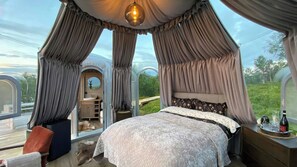 A bedroom with a canopy bed, a round mirror, and a view of the outdoors.
