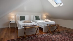 A bedroom with two beds, a small table, a nightstand, and a patterned rug. - Villa with pool in Machico near beach|Casa da Tia (Machico)