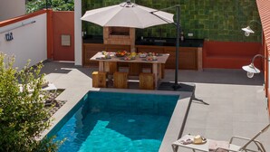 A poolside area with a barbecue setup, a table with food and drinks, and lounge chairs. - Villa with pool in Machico near beach|Casa da Tia (Machico)