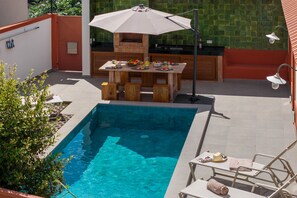 Ein Poolbereich mit Grillmöglichkeit, einem Tisch mit Speisen und Getränken sowie Liegestühlen.