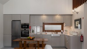 A modern kitchen with grey cabinets, a wooden dining table, and a built-in oven. - Villa with pool in Machico near beach|Casa da Tia (Machico)