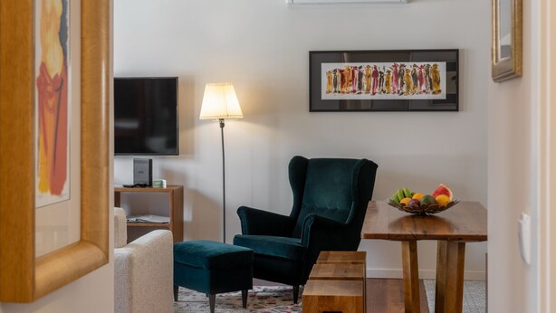 A living room with a dark green armchair, a small wooden table with a fruit bowl, a floor lamp, a flat-screen TV, and a framed abstract painting on the wall. - Villa with pool in Machico near beach|Casa da Tia (Machico)