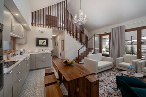 Eine moderne Küche mit einer Holztreppe, einem Essbereich mit einem Holztisch und einem Wohnzimmer mit einer Couch und Sesseln.