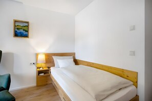 A hotel room with a wooden headboard, a single bed, a bedside table with a lamp, and a painting on the wall. - Apartment 3 – Single Apartment with Well-Equipped Kitchen and Private Bathroom (Kirchseeon)