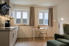 Eine kleine Küche mit einer Kaffeemaschine, einem Esstisch mit einem Stuhl und einem grünen Sofa.