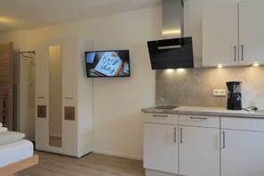 A modern kitchen with white cabinetry, a built-in oven, a coffee maker, and a flat-screen TV displaying a birthday greeting. - Apartment 3 – Single Apartment with Well-Equipped Kitchen and Private Bathroom (Kirchseeon)