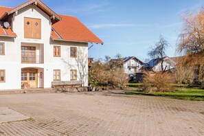 A large white building with a red-tiled roof, multiple windows, and a paved courtyard. - Apartment 3 – Single Apartment with Well-Equipped Kitchen and Private Bathroom (Kirchseeon)