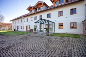 A multi-story building with a covered entrance, a paved courtyard, and a grassy area. - Apartment 3 – Single Apartment with Well-Equipped Kitchen and Private Bathroom (Kirchseeon)