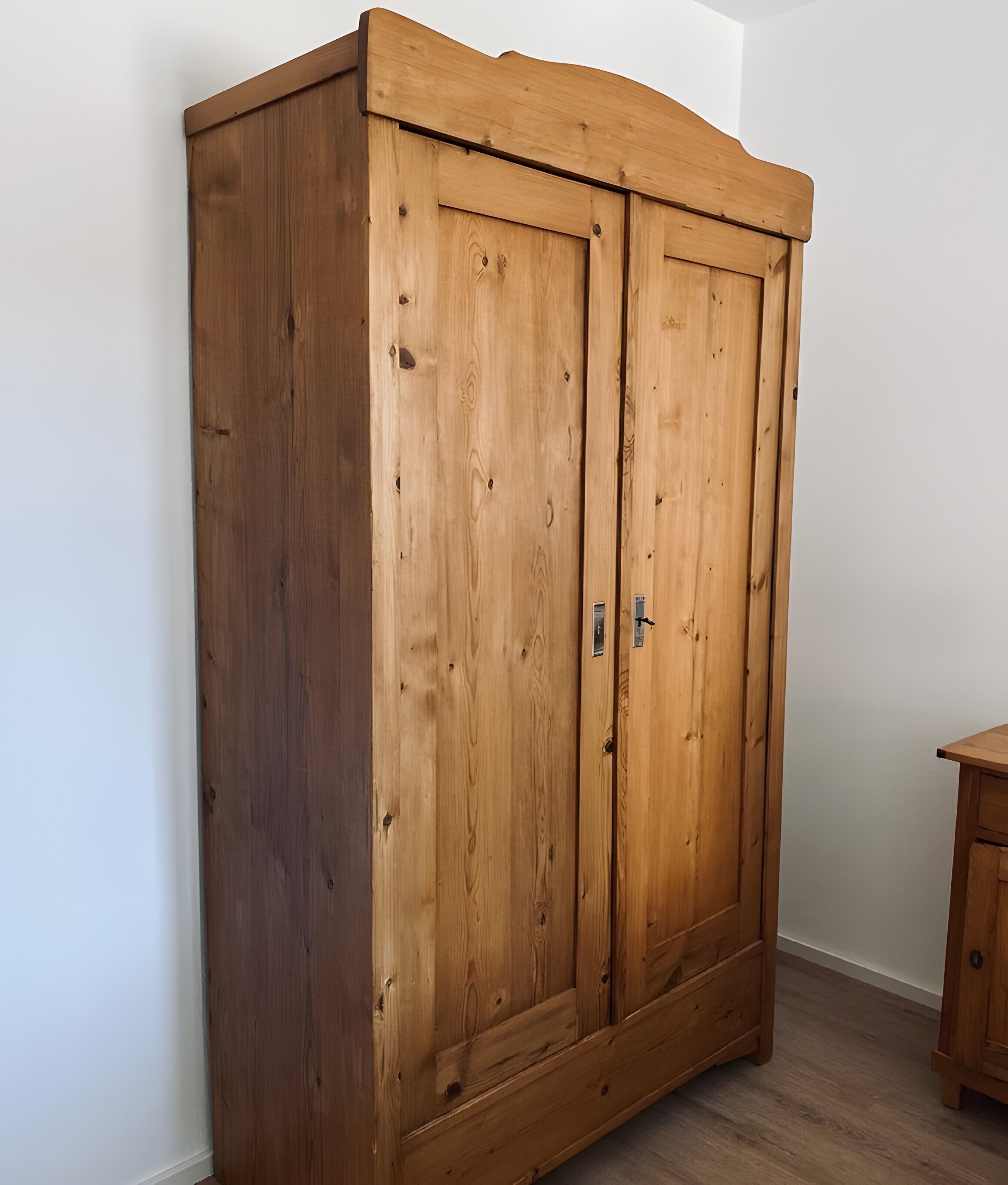 A wooden wardrobe with two doors and a small cabinet beside it.