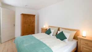 A bedroom with a bed, two bedside tables with lamps, a wooden wardrobe, and a door. - Apartment 5 – Well-Equipped Kitchen, Spacious Outdoor Area, and Beautiful Nature Views (Kirchseeon)