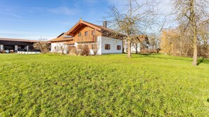 A two-story wooden house with a sloped roof, surrounded by a well-maintained grassy field. - Apartment 5 – Well-Equipped Kitchen, Spacious Outdoor Area, and Beautiful Nature Views (Kirchseeon)