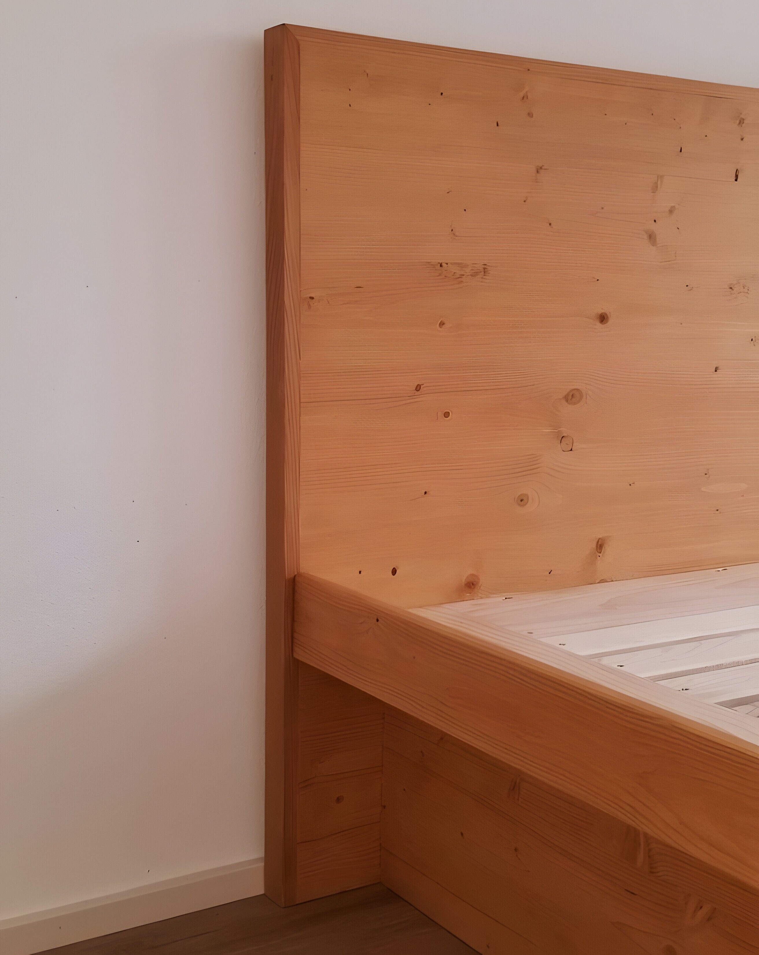 Ein Bettgestell aus Holz mit querverlaufenden Kopf- und Fußstücken, an einer schlichten Wand platziert.