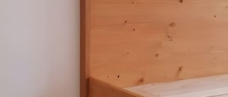 Ein Bettgestell aus Holz mit querverlaufenden Kopf- und Fußstücken, an einer schlichten Wand platziert.
