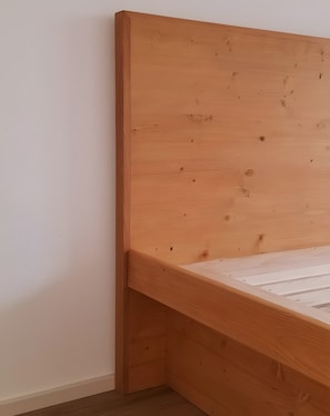 Ein Bettgestell aus Holz mit querverlaufenden Kopf- und Fußstücken, an einer schlichten Wand platziert.