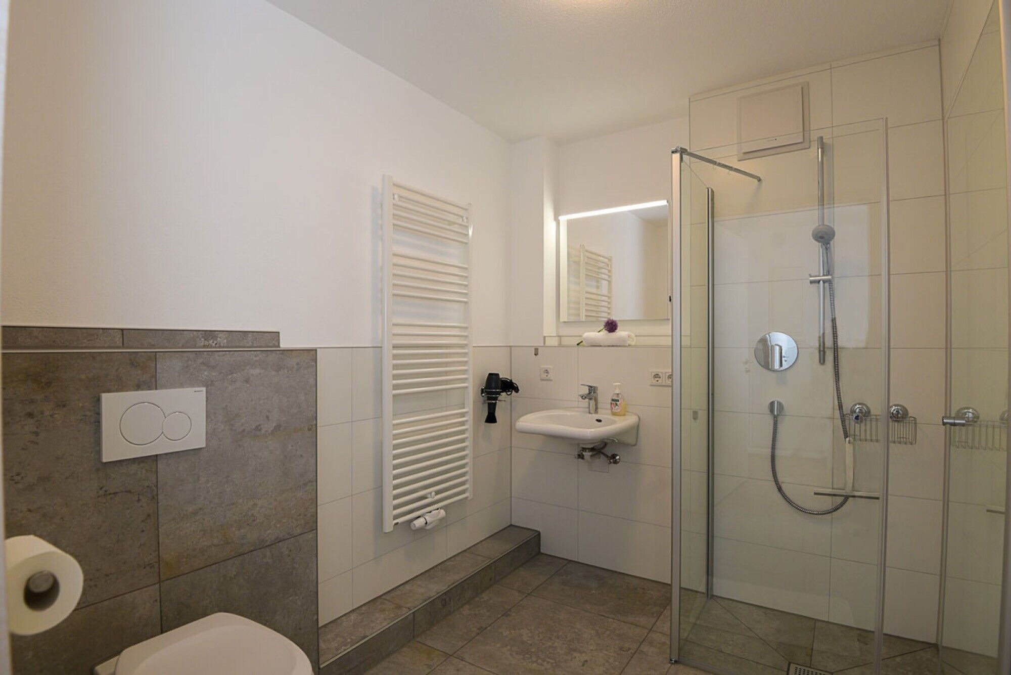 Ein modernes Badezimmer mit einer Duschkabine, einem weißen Waschbecken und einer Toilette.