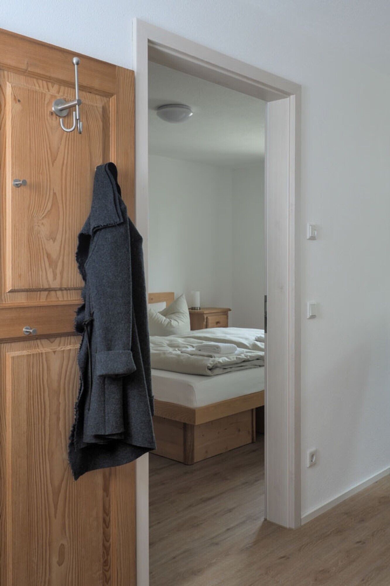 A bedroom with a wooden wardrobe, a bed with white bedding, and a nightstand with a lamp.