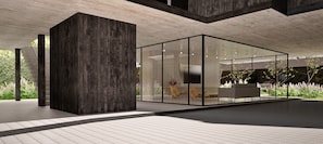 A modern interior with a glass partition, a large dark wooden column, and a seating area with a sofa and chairs.