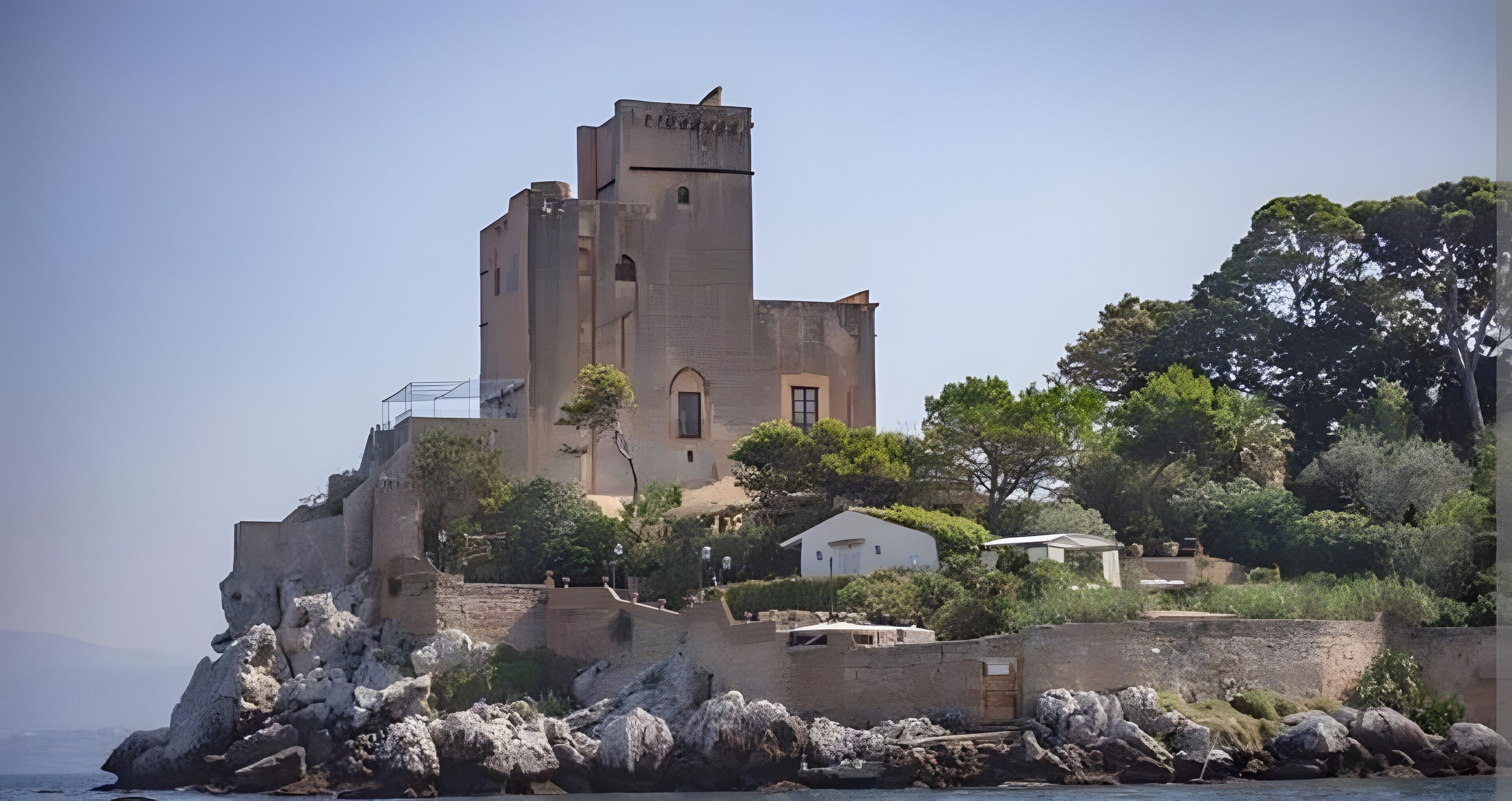 A coastal building with a tower, surrounded by vegetation and rocky terrain.