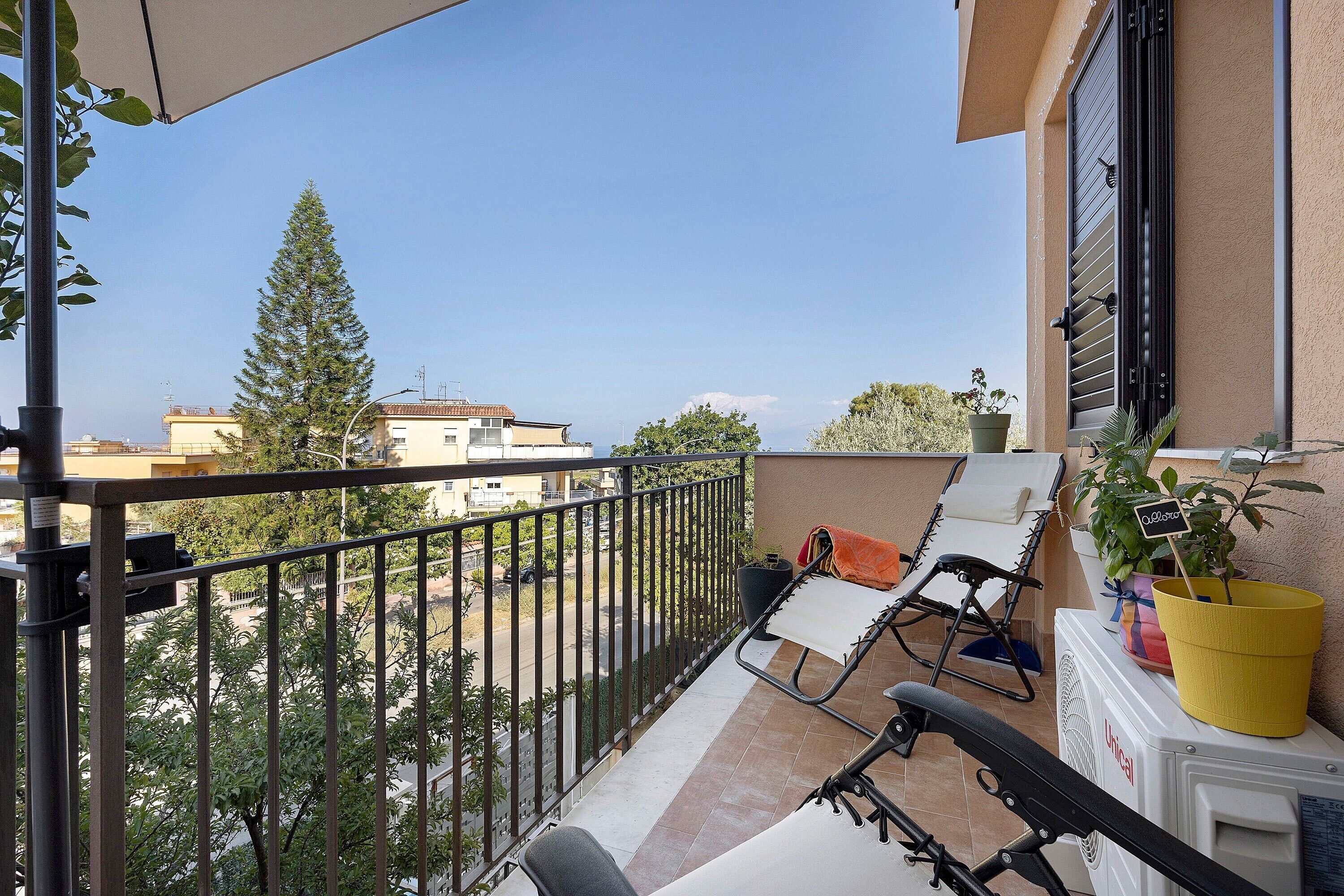 Un balcone con vista sulla città, una sedia, un tavolino e una pianta in vaso.